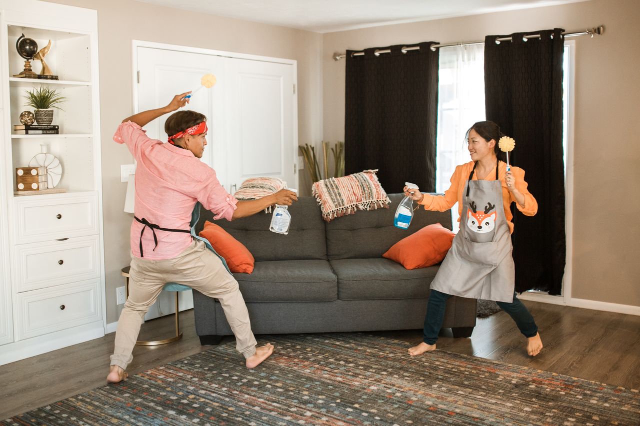 A cheerful couple is having a playful cleaning tussle in their living room, highlighting a lighthearted everyday home moment.