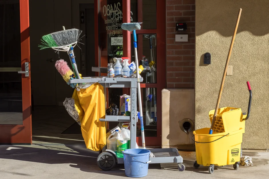 An adult woman in red coveralls operates a vacuum cleaner in a modern indoor setting, focusing on cleaning tasks.